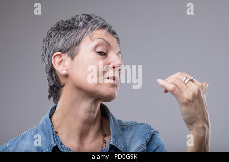 Elegant diva style woman with supercilious look glancing sideways at the camera as she gestures with her hand isolated on grey Stock Photo