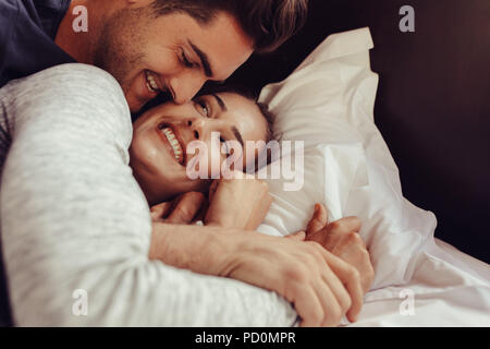 Smiling young couple lying together on bed. Romantic young couple lying in bed. Stock Photo