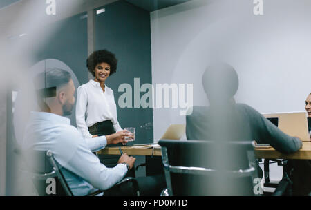 African business woman conducting a presentation for business colleagues in boardroom. Group of business professionals sitting inside conference room  Stock Photo