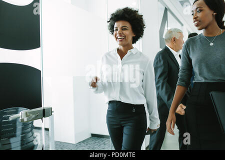 Smiling young woman with colleagues walking through office corridor. Business professional walking through office hallway and smiling. Stock Photo