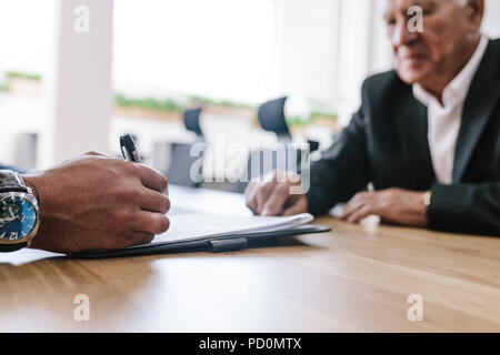 Hand of young man signing contract with senior man sitting around the table. Business people signing contract papers in office. Stock Photo