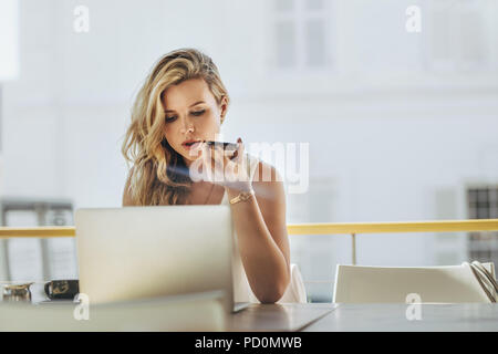 Young businesswoman sitting at cafe having telephonic conversation with client. Woman working on laptop and talking on mobile phone. Stock Photo