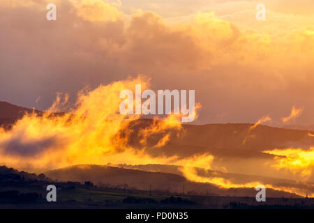 Low clouds in backlight over a rolling landscape at sunset Stock Photo