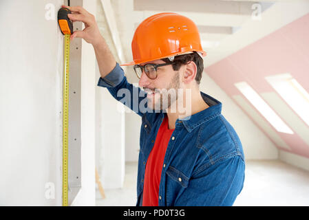 Portrait of young man using measuring tape while working on construction site. Stock Photo