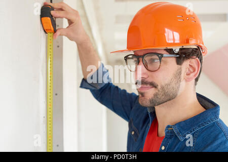 Close-up portrait of young man using measuring tape while working on construction site. Stock Photo