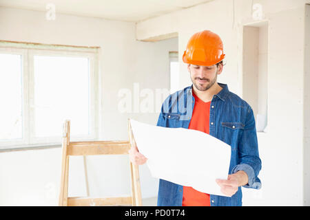 Portrait of young male engineer holding blueprint in his hand while standing at construciton site. Stock Photo