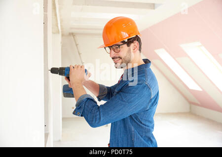 Successful young handyman using hammer drill driver at construction site. Stock Photo