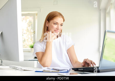Shot of smiling young businesswoman looking thoughtully while using her laptop at the office. Stock Photo