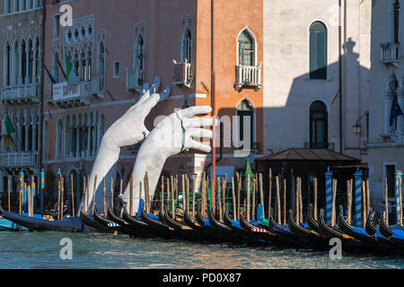 Venice, Italy - March 22, 2018: Giant hands rise from the water of Grand Canal to support the building in Venice. This powerful report on climate chan Stock Photo