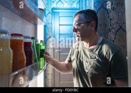 Middle-aged casual man searching for a bottle of beverage in the door of a fridge with a point of view from inside the refrigerator Stock Photo