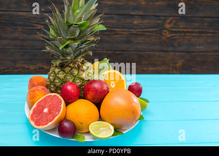 Plate of colorful healthy fresh tropical fruit with assorted citrus, nectarines, pineapple and plums on a turquoise blue table with copy space Stock Photo