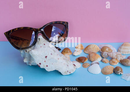 A women's sunglasses over a large shell and several smaller shells on a light blue and pink background. Minimalist nice image that capture the spirit  Stock Photo