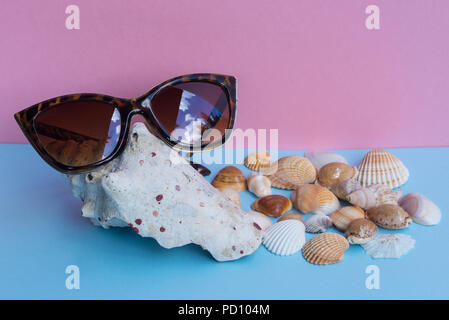 A women's sunglasses over a large shell and several smaller shells on a light blue and pink background. Minimalist nice image that capture the spirit  Stock Photo