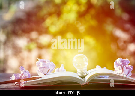 Creative thinking, idea, business concept : Light bulb put on open notebook with crumpled papers and pencil on wooden table with green nature as backg Stock Photo