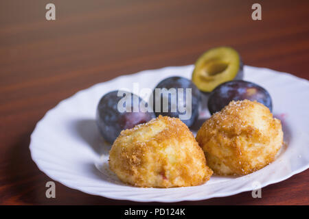 Fresh plum dumplings. Two dumplings with fresh plums on white plate on dark red table. Stock Photo