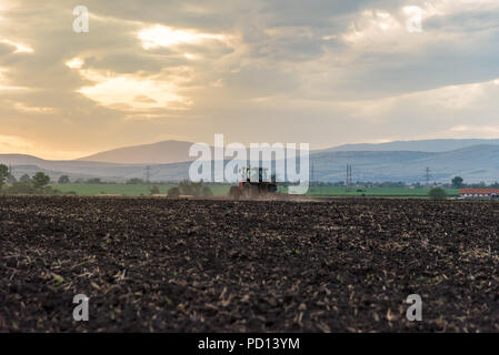 Farming tractor plowing and spraying on field. Stock Photo