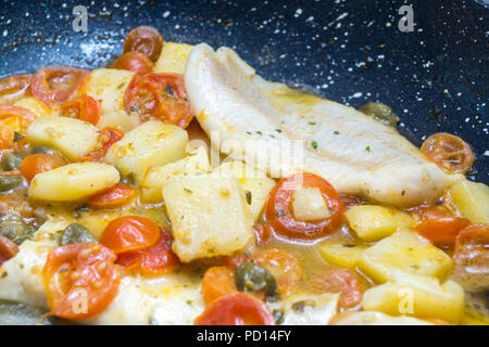cod cooked in a pan, with tomato, potatoes and capers Stock Photo