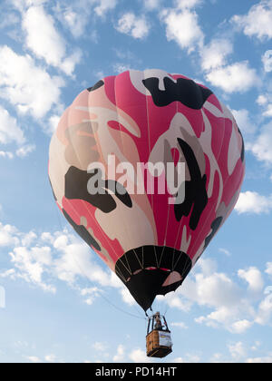 A pink camouflage hot air balloon in flight against blue sky and fluffy white clouds. Stock Photo