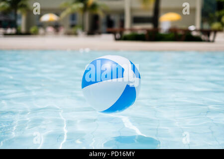 Blue and white inflatable ball floating on swimming pool under the summer sun. Stock Photo