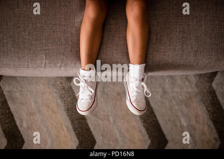 Little girls legs on sofa with white shoes with red details. Symmetrical  pattern on carpet, everything is grey Stock Photo - Alamy