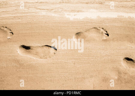Adult footprints on wet white sandy coast. No people. Water not visible. Closeup horizontal view Stock Photo