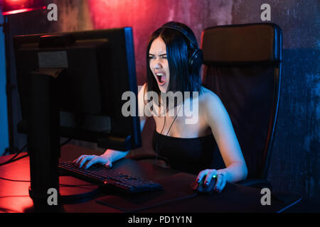Screaming emotional young angry woman playing on personal computer holding game keyboard and mouse sitting on a chair at home. Gaming gamers concept. Stock Photo