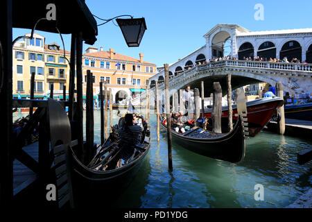 Two gondolas getting ready for a ride on the Grand Canal in Venice, while tourists watching the scene from the Rialto Bridge in the background Stock Photo