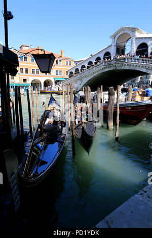 Two gondolas getting ready for a ride on the Grand Canal in Venice, while tourists watching the scene from the Rialto Bridge in the background Stock Photo