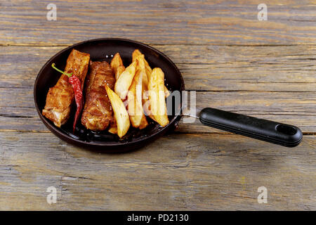Fried ribs with potatoes in a frying pan on a wooden rustic table. Close up and selective focus. on a plate on a low fat healthy eating concept. Stock Photo