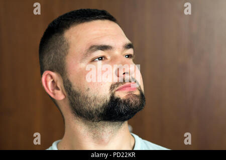 Portrait of handsome bearded confident intelligent modern photogenic young man with short haircut and black eyes looking thoughtfully ahead on blurred Stock Photo