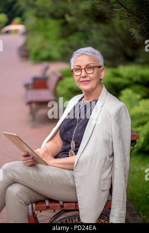 an active mature woman looking at the camera. elderly teacher resting on the alley Stock Photo
