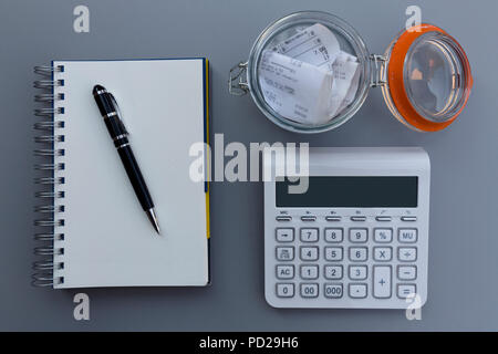 Personal expense and cost balance calculation concept, pen on the notebook, receipts in the jar and calculator on wooden table. Stock Photo