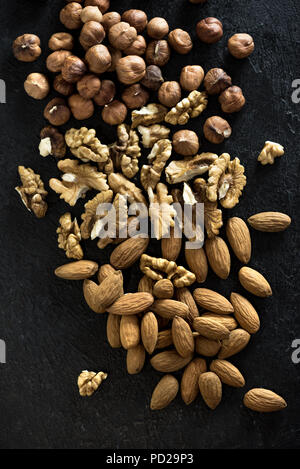 Organic Nuts. Various nuts (walnuts, hazelnuts, almonds)  on black stone background, top view, copy space. Stock Photo