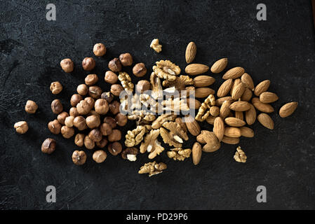 Organic Nuts. Various nuts (walnuts, hazelnuts, almonds)  on black stone background, top view, copy space. Stock Photo