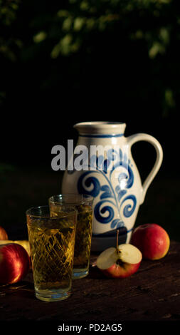 Traditional apple wine in the city of Frankfurt in Hesse. A jug of wine is on an old wooden table in the garden, around it are apples Stock Photo