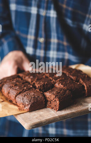 Freshly baked brownies on wooden serving board. Hands holding tray with brownies Stock Photo