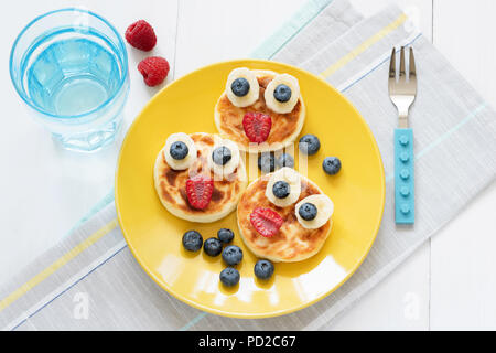 Breakfast for kids. Funny animal face pancakes with fresh berries on yellow plate and glass of pure still water. Top view Stock Photo