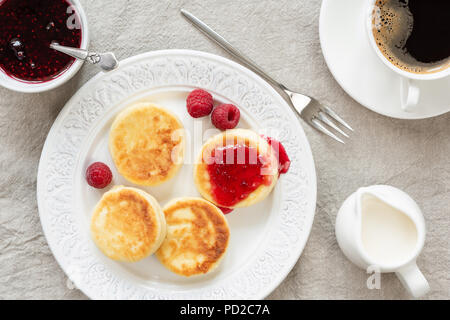 Cottage cheese pancakes with jam and coffee. Russian syrniki or sirniki, cottage cheese fritters or pancakes served with raspberry jam and cup of coff Stock Photo