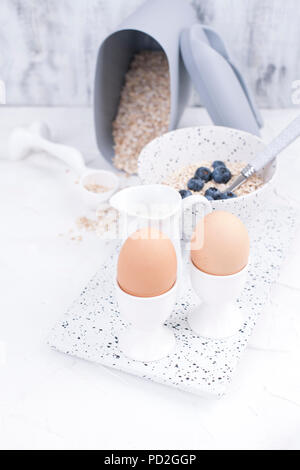 Boiled eggs for breakfast, oatmeal porridge with berries and milk in white dishes on a light background. Delicious and healthy breakfast. Free space for text. Top view. Copy space Stock Photo