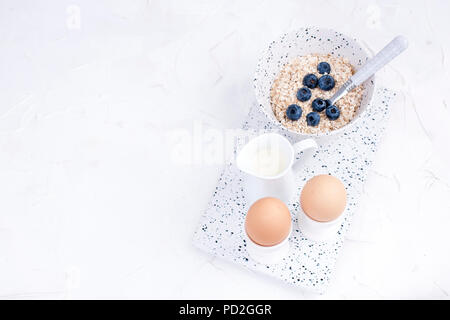 Boiled eggs for breakfast, oatmeal porridge and milk in white dishes on a light background. Delicious and healthy breakfast. Free space for text. Top view. Copy space Stock Photo
