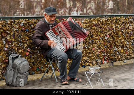 Paris, France - July 21, 2014: Old man on a stool playing accordion for tips on Pont des Arts Bridge – a bridge over River Seine in Paris. Stock Photo