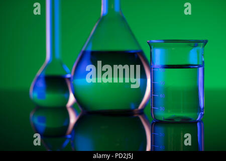 Chemical laboratory concept. Experiment with liquids. Laboratory glassware.   Green or red background. Place for logo. Stock Photo