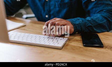 Close up of young man hands typing on computer keyboard on his desk. Cropped shot of business man working on computer on office desk. Stock Photo