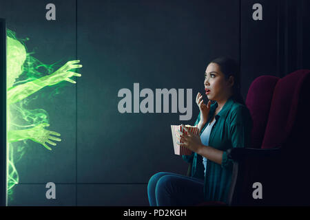 Shocked asian woman watching scary movie with popcorn at home Stock Photo