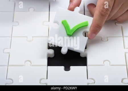 Human hand solving jigsaw puzzle by connecting white piece with check mark Stock Photo