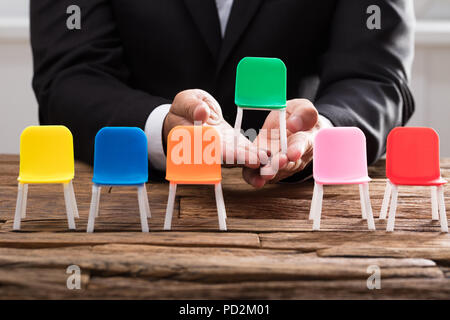 Businessperson's hand picking up green chair among others on wooden desk Stock Photo