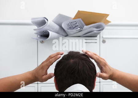 Close-up of man with hand on head in front of overloaded mailbox with junk mail Stock Photo