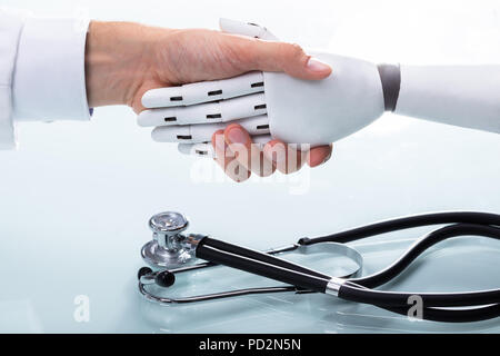 Doctor And Robot Shaking Hands Over Stethoscope Stock Photo