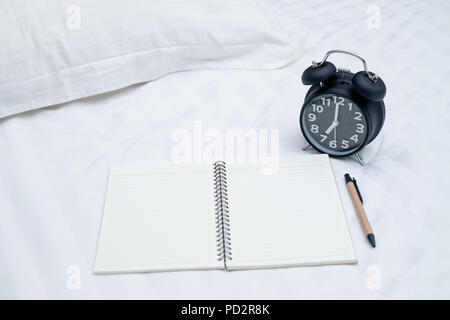 Diary or notebook and vintage alarm clock on bed in bedroom at home or hotel, working or note something before sleep. Stock Photo