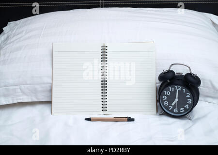 Diary or notebook and vintage alarm clock on bed in bedroom at home or hotel, working or note something before sleep. Stock Photo
